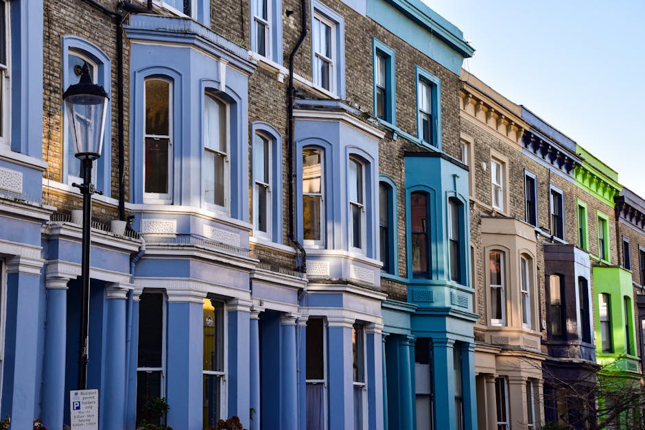 A narrow street lined with red brick Victorian terrace houses featuring decorative cornices, bay windows, and small balconies. The pavement is paved with cobblestones, and there are yellow road markin